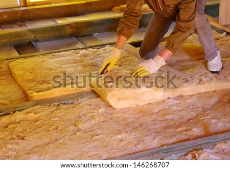 Construction worker thermally insulating house attic with glass wool
