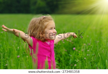 Cute little girl on the meadow in spring day. Child running on field . Child with arms outstretched. Freedom concept.