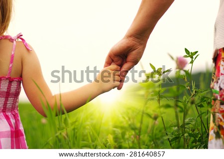 Hands of mother and daughter holding each other on field