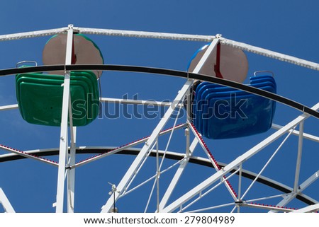 Upper part of ferris wheel with green and blue bowls against blue sky