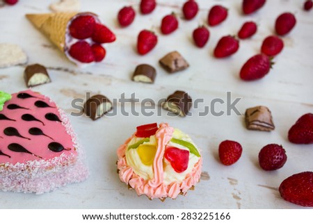 Confectionery: strawberry ice cream, fruit cake, chocolate candy, strawberry, cherry and biscuits on the table