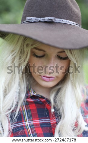 Beautiful healthy young woman outdoors wearing a big floppy hat and a checked shirt