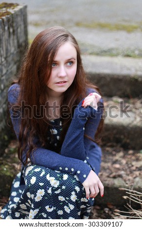 young woman with long brown wavy hair sitting on a steps outdoors