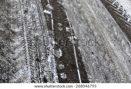 Traces of tires of various vehicles and soles on asphalt during easy snowfall.