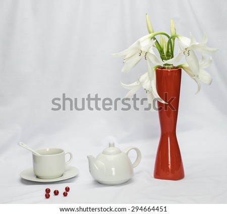 Red vase with flowers, teapot, cup and saucer and spoon on a white cloth.