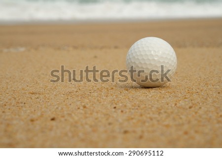 Golf ball on sand with the ocean background