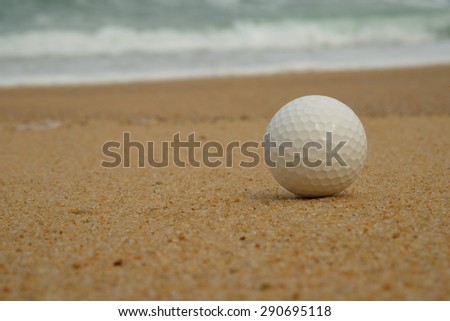 Golf ball on sand with the ocean background