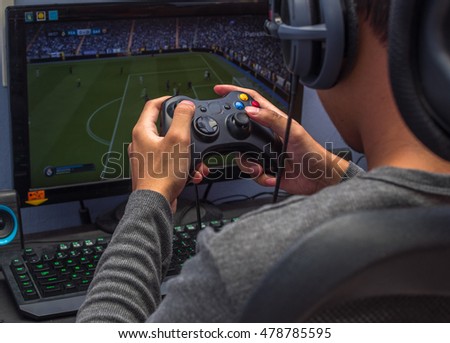 Back view of young gamer playing video game wearing headphone using his controller.