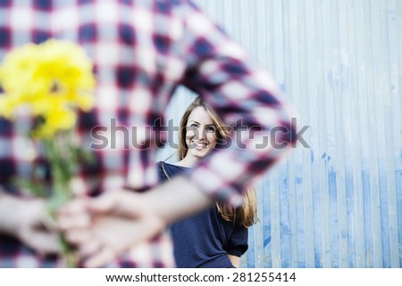 Beautiful flowers for her. Rear view of young man holding yellow flowers behind his back while woman smiling in the background