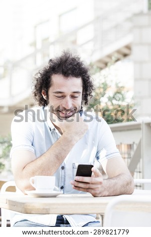 Handsome man watching social media in a smart phone in a restaurant terrace