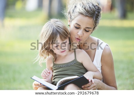 Mother with daughter reading a book in the park