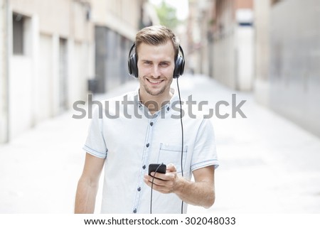 Happy guy walking and using a smart phone to listen music with headphones