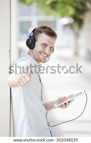 Happy guy walking and using a tablet to listen music with headphones