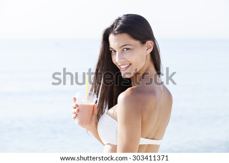 Cold smoothie - portrait of a woman drinking smoothie in bikini at beach. Healthy lifestyle concept
