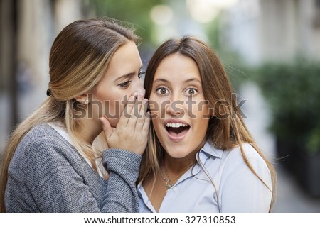 Attractive young woman whispering secret in friend\'s ear