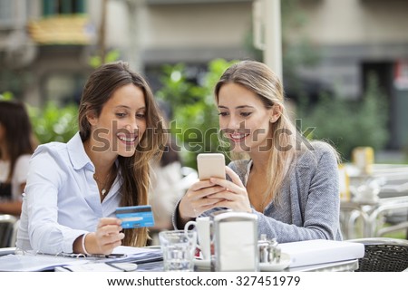 Friends buying on-line with phone and credit card on terrace bar
