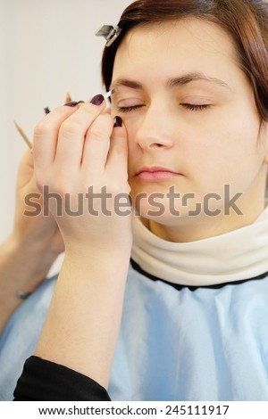 Makeup artist stylist applying with brush cosmetic on eyebrow of a beautiful woman