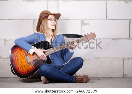 woman in a hat plays guitar sitting on the floor