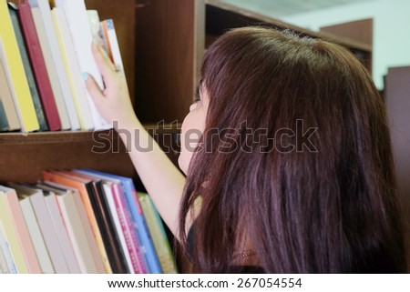 Beautiful Woman in the library takes the book from the shelf