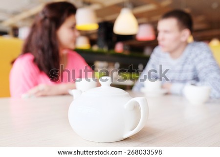 Closeup white kettle. Beautiful young couple drinking tea in cafe