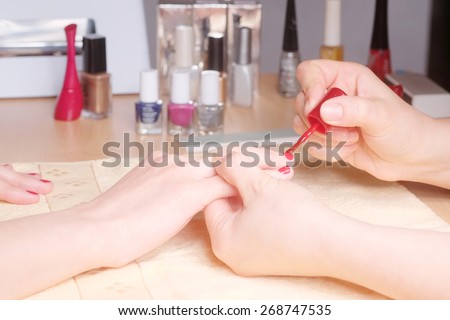 Manicurist doing manicure client painting nails with red nail polish in salon on yellow towel