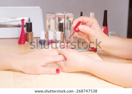 Manicurist doing manicure client painting nails with red nail polish in salon on yellow towel