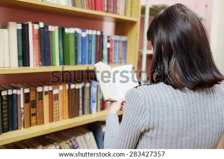 Back view woman in a library with book at self-education