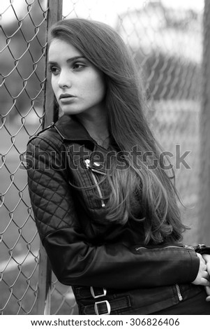 Fashionable black and white photo from a magazine. beautiful young rocker in a heavy leather jacket, with long beautiful black hair posing on the background grid and Park