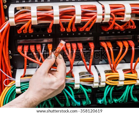 Close up of hand with red network cable and cables connected to black patch panel