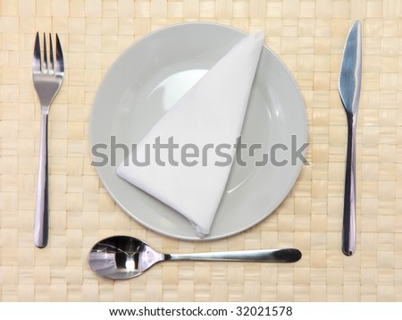 Table appointments- plate,spoon,  fork,knife, silk napkin   on beige wicker bamboo mat. Isolated around.