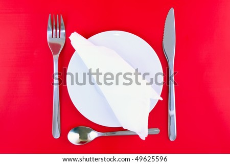 Table serving- knife, spoon, fork and silk napkin  on red  backgroung.