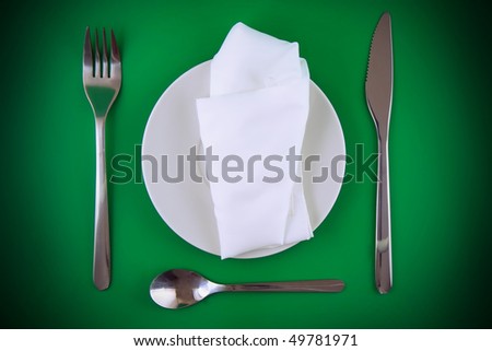 Table serving-knife, fork , spoon and silk napkin on green  background.Spotlight source on top and in center.