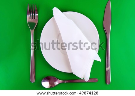 Table serving- knife, spoon, fork, spoon and silk napkin  a on  green   background.