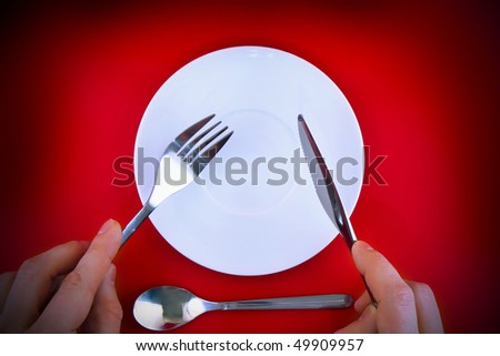 Table serving-knife, fork in hands and spoon  on red  background.Spotlight source on top and in center.