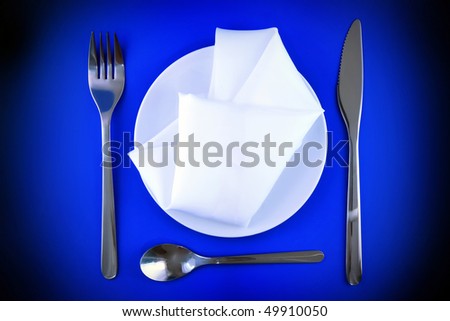 Table serving-knife, fork, spoon  and silk napkin on blue  background.Spotlight source on top and in center.
