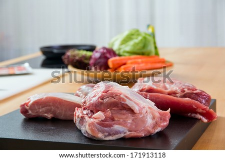Meat parts on the table with vegetables at background