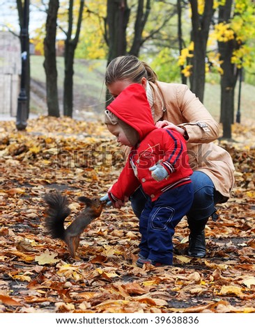 Little boy with mother feeds a squirrel in a park