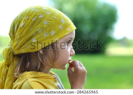 A little girl in a bright yellow bandanna eating a biscuit, close up