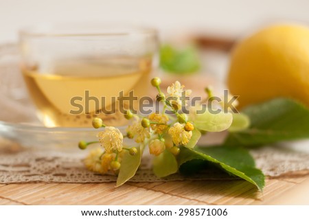 A glass cup of lime flower tea, fresh lemon tea blossom and a ripe lemon on a wooden surface