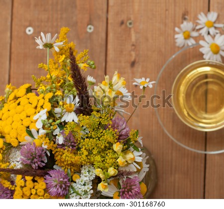 A bouquet of field summer flowers and a cup of chamomile tea in a glass cup on a wooden surface, top view