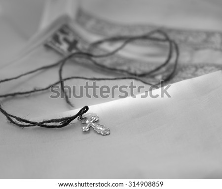 A cotton baptismal shirt for a new born baby and a cross on a coarse string placed on it,  black and white photo
