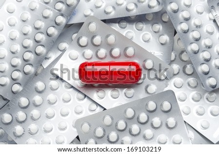 Medication. Giant red pill on smaller white pills in blister packs.