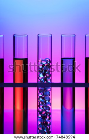 Test tubes filled with colored fluid, one filled with gel cap vitamins.