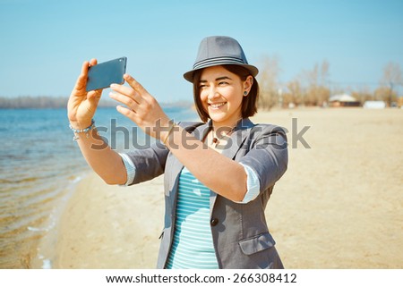 young woman on the sea beach at the morning. woman dressed in sneakers jeans jacket and hat. She is taking a selfie