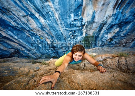 female rock climber climbs on a rocky wall, Keep a hand on the rock and laughs.