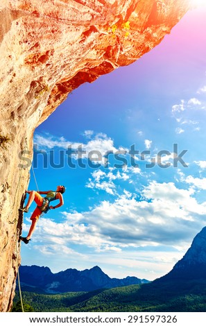 female rock climber climbs on a rocky wall against a blue cloudy sky