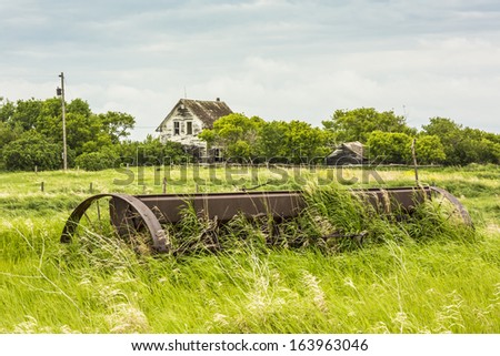 An old abandoned house on a farm yard with rusty farm machinery in the grass