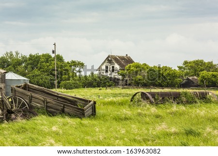 An old abandoned house on a farm yard with rusty farm machinery in the grass