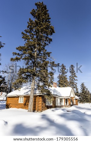 Snow covered log cabin between the trees in winter