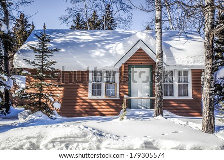 Snow covered log cabin between the trees in winter